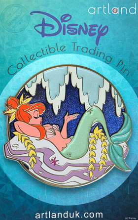 A collectible pin featuring a mermaid character from the Peter Pan series, depicted reclining on a rock with a metallic blue background and shimmering enamel detailing.